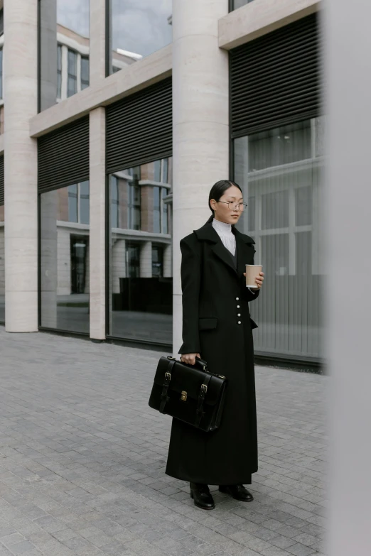 a woman standing in front of a building holding a briefcase, pexels contest winner, wearing black coat, avant designer uniform, mei-ling zhou, ready for a meeting