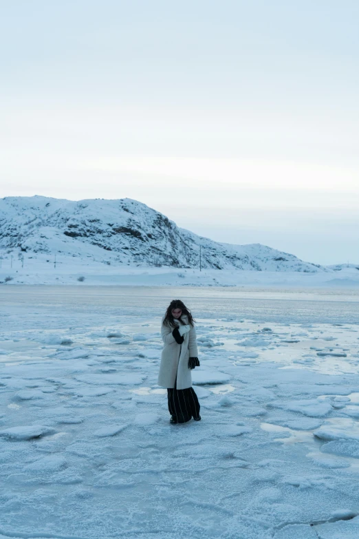 a woman standing in the middle of a frozen lake, inspired by Louisa Matthíasdóttir, happening, glacier, fashionable, looking serious, standing near the beach