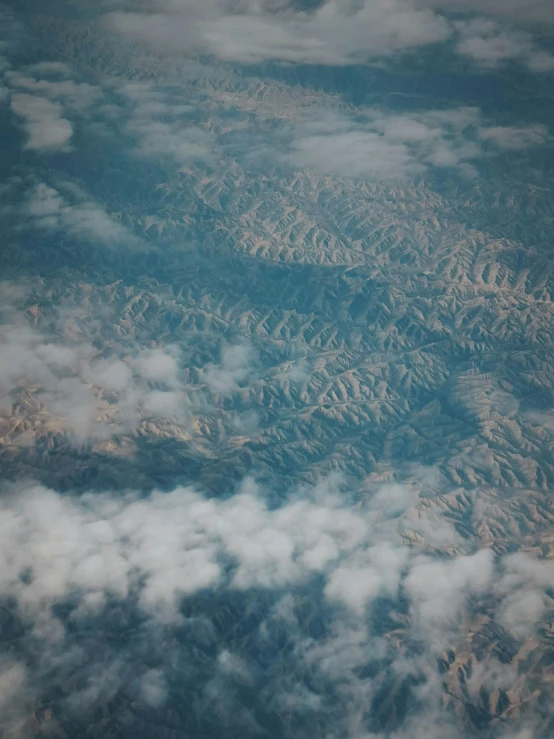 a view of mountains and clouds from an airplane, an album cover, trending on unsplash, erosion algorithm landscape, low quality photo, grain”, intricate image