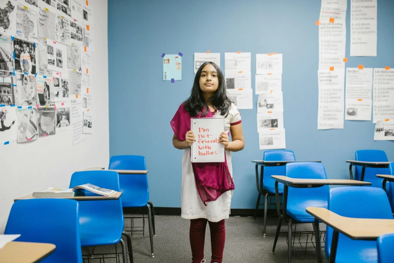 a girl standing in a classroom holding a sign, an album cover, pexels contest winner, hindu, bay area, basia tran, thumbnail