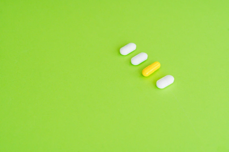 a couple of pills sitting on top of a green surface, antipodeans, white and yellow scheme, lined up horizontally, three, with a long white