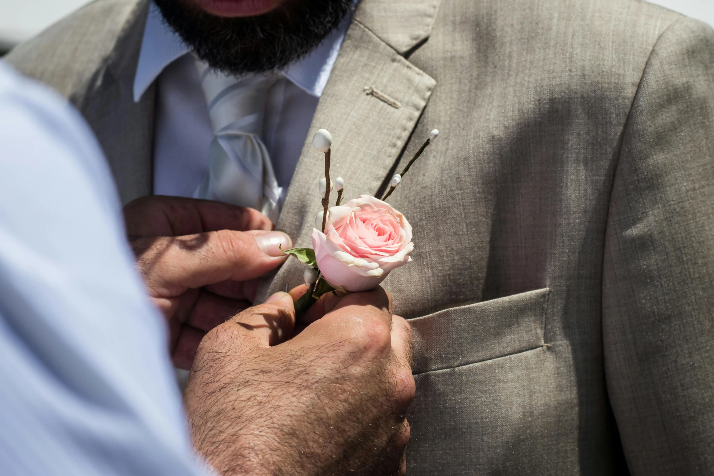 a man in a suit putting a flower on his lapel, a colorized photo, by Niko Henrichon, pexels contest winner, stick poke, natural point rose', wearing a grey robe, wedding