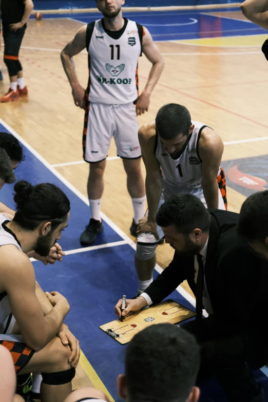 a group of men sitting on top of a basketball court, sam nassour, charts, head down, start of the match