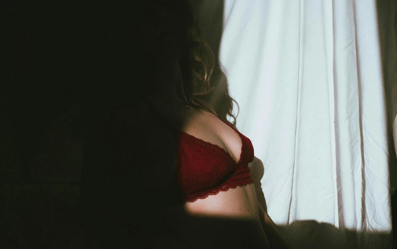 a woman in a red lingerie standing in front of a window, inspired by Elsa Bleda, unsplash contest winner, low quality grainy, someone sits in bed, wearing bra, light and shadow