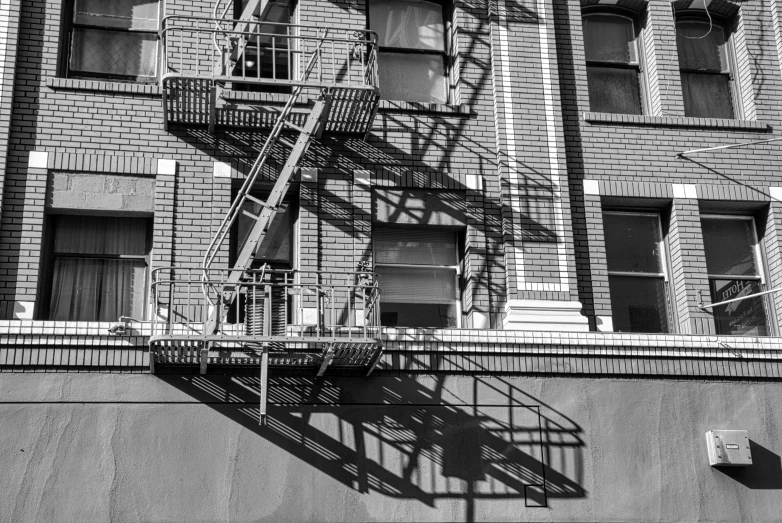 a black and white photo of a fire escape ladder, a black and white photo, inspired by André Kertész, pexels, op art, dappled afternoon sunlight, deep shadows and colors, reflective windows, long shadow