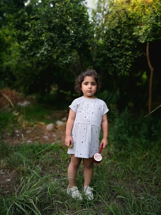 a little girl that is standing in the grass, a picture, by Lucia Peka, tiny stars, standing in the forrest, ameera al taweel, grey