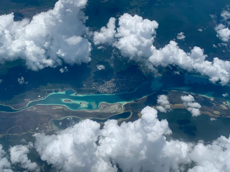 an aerial view of a body of water surrounded by clouds, by Daren Bader, pexels contest winner, hurufiyya, tropical coastal city, carribean turquoise water, airplane window view, complex and intricate