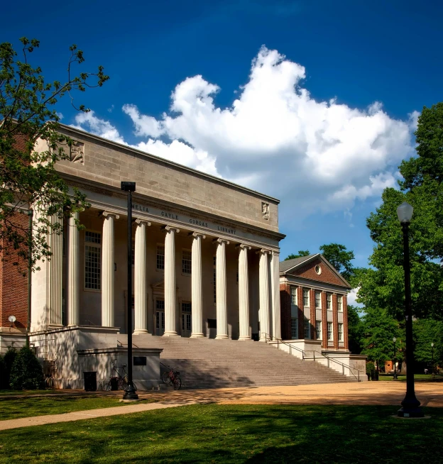 a large building sitting on top of a lush green field, unsplash, academic art, memphis, steps, on a sunny day, old library