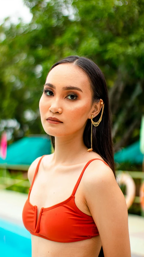 a woman standing next to a swimming pool, an album cover, inspired by Ruth Jên, trending on pexels, sumatraism, long earrings, asian beautiful face, gold earring, headshot
