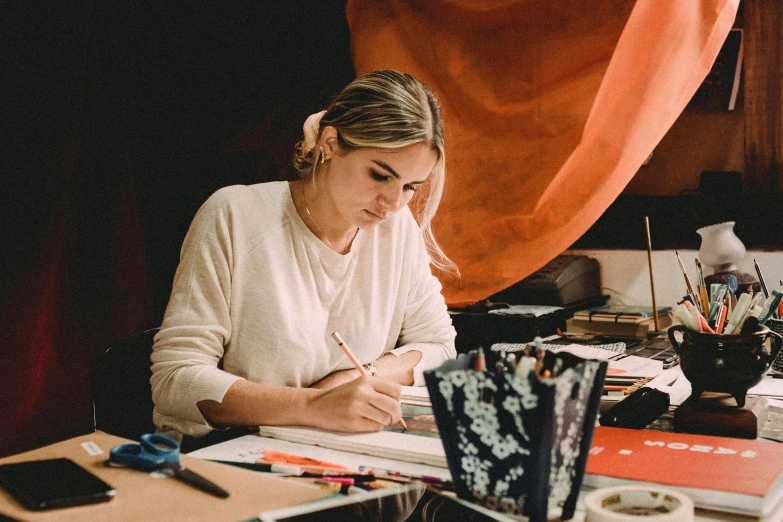 a woman sitting at a desk writing on a piece of paper, a drawing, by Lee Loughridge, pexels contest winner, samara weaving, artisanal art, lachlan bailey, jen bartel