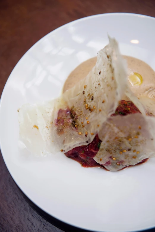 a white plate topped with food on top of a wooden table, a picture, ignant, folded, gooey skin, andrew bernstein