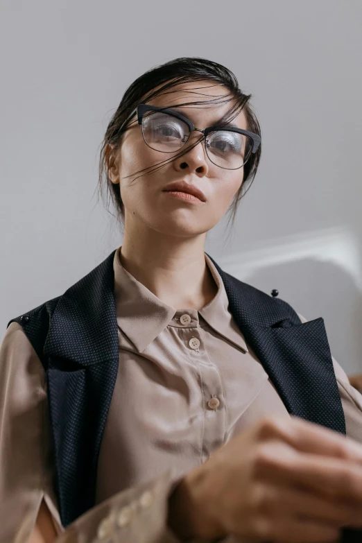 a woman sitting in front of a laptop computer, a character portrait, inspired by Ruth Jên, trending on pexels, in square-rimmed glasses, model is wearing techtical vest, vietnamese woman, serious look