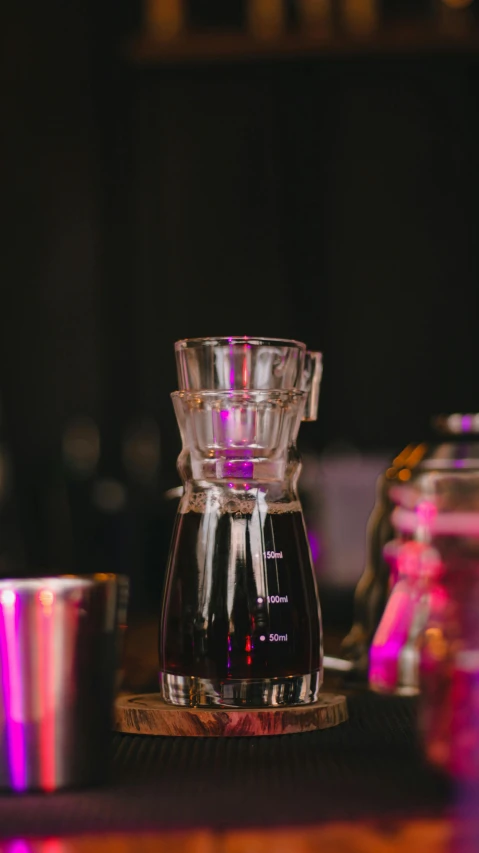 a coffee maker sitting on top of a wooden table, a still life, by Robbie Trevino, unsplash, barely lit warm violet red light, glassware, thumbnail, museum quality photo