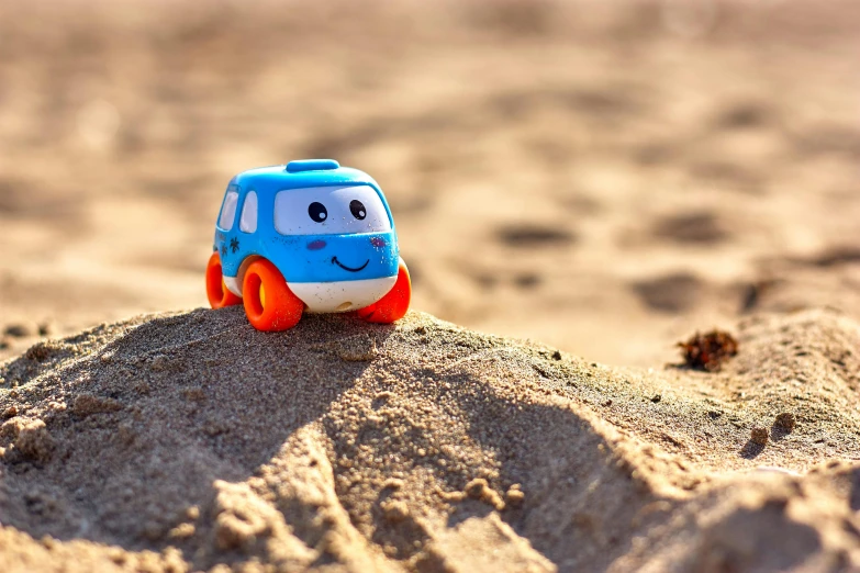 a toy car sitting on top of a sandy beach, blue and orange, squishy, warm friendly expression, soft-sanded coastlines