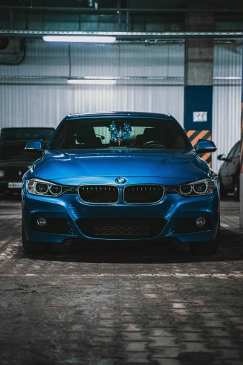 a blue car parked in a parking garage, by Adam Marczyński, pexels contest winner, bmw, good looking face, aftermarket parts, front side