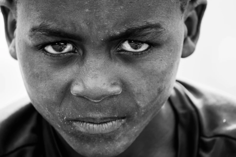a black and white photo of a young boy, by John Hutton, pexels contest winner, african facial features, fierce eyes, teenage boy, diverse eyes!
