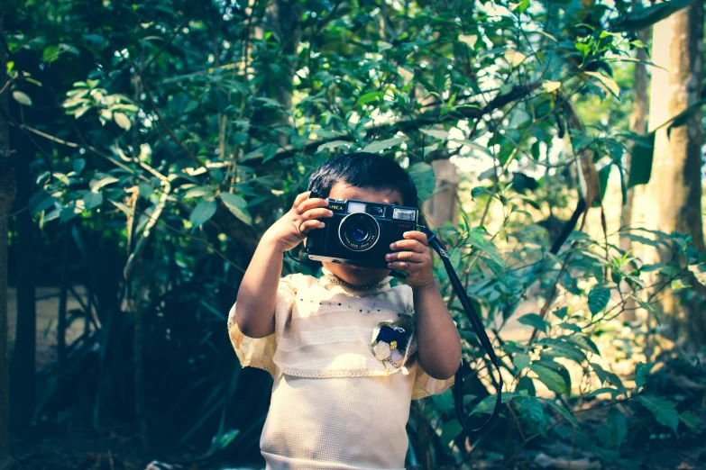 a young boy taking a picture with a camera, inspired by Steve McCurry, unsplash, visual art, on a jungle forest, toddler, retro stylised, avatar image