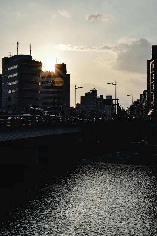 a river running through a city next to tall buildings, a picture, unsplash, shin hanga, silhouette :7, sun and shadow, kumamoto, fujifilm”