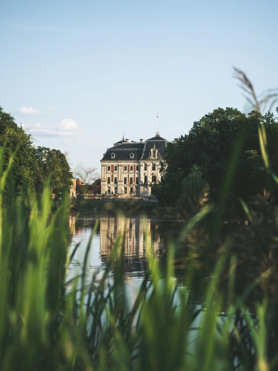 a large building sitting on top of a lush green field, pexels contest winner, heidelberg school, view from the lake, screenshots, rococo details, warm light