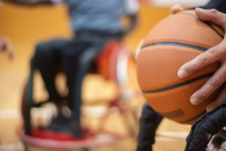 a person in a wheelchair holding a basketball, person in foreground, schools, zoomed in, game ready