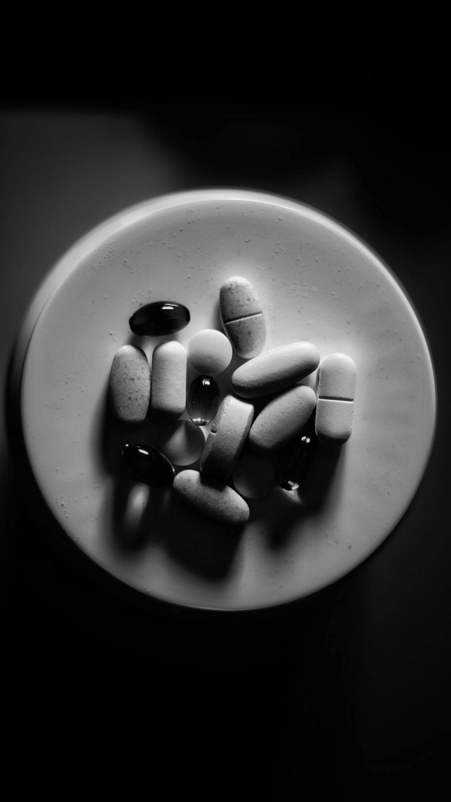 a white plate topped with pills on top of a table, a black and white photo, by Adam Chmielowski, on flickr in 2007, alien capsules, dark and dim, uploaded