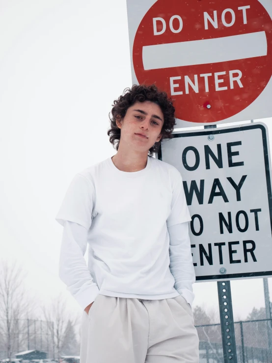 a man standing in front of a do not enter sign, an album cover, by Grace Polit, pexels contest winner, portrait of timothee chalamet, wearing a white sweater, highways, white clothing