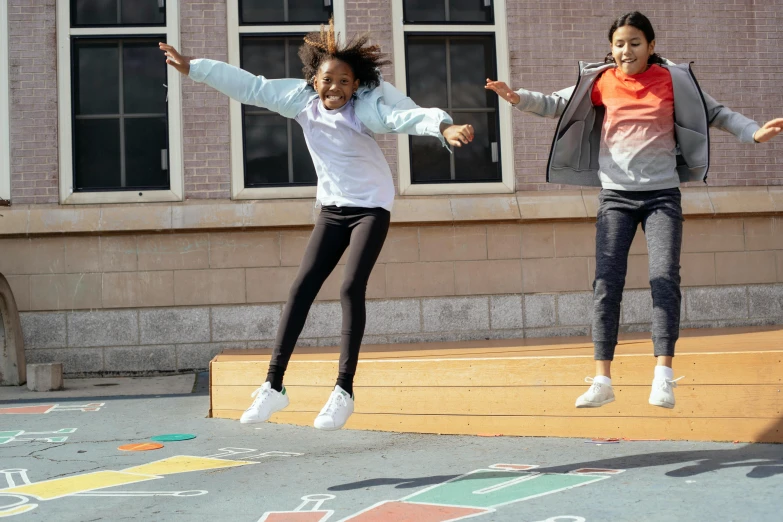 two girls jumping in the air in front of a building, platform game, school courtyard, promotional image, multicoloured