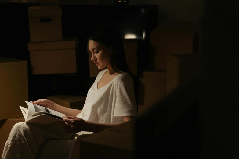 a woman sitting in a chair reading a book, light and space, inspect in inventory image, no lights in bedroom, cardboard, an asian woman