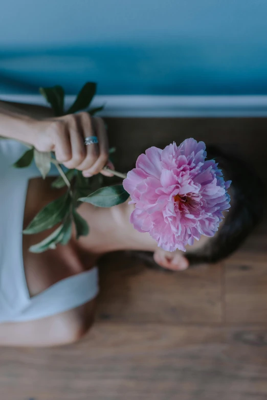 a woman laying on the floor with a flower in her hand, inspired by Elsa Bleda, pexels contest winner, peony, standing, meditative, giant carnation flower as a head