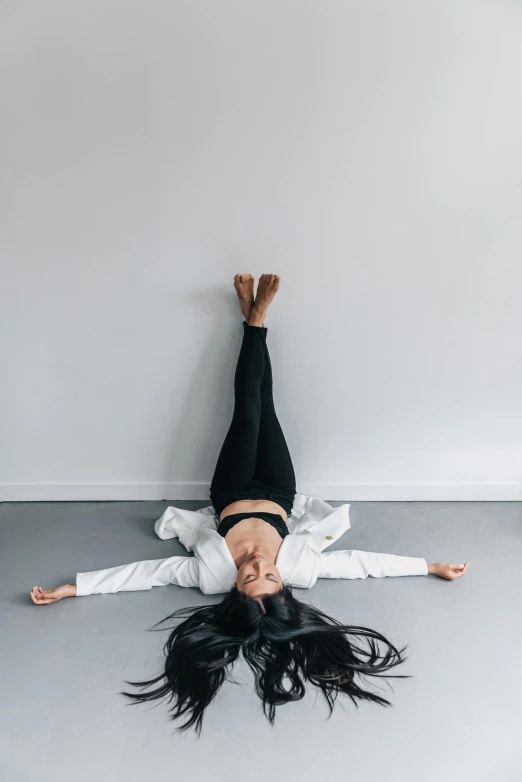 a woman laying on her back on the floor, trending on unsplash, arabesque, broken down grey wall, in front of white back drop, with arms up, high angle