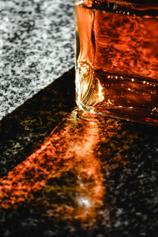 a glass filled with liquid sitting on top of a counter, an album cover, unsplash, photorealism, black and orange, whiskey, texture detail, dappled sunlight