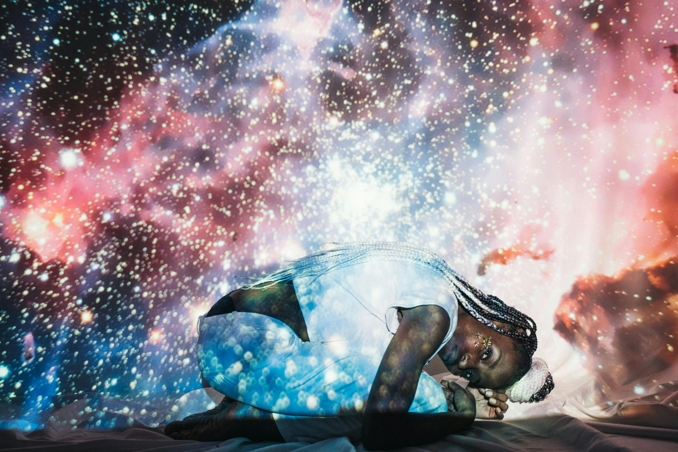 a man laying on top of a bed under a sky full of stars, an album cover, by Chinwe Chukwuogo-Roy, magical realism, cosmic bjork, fireworks, covered in crystals and glitter, little girl with magical powers