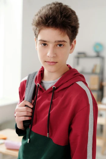 a young boy with a backpack standing in a classroom, inspired by John Luke, trending on pexels, photorealism, wearing a track suit, acting headshot, androgynous person, red shirt