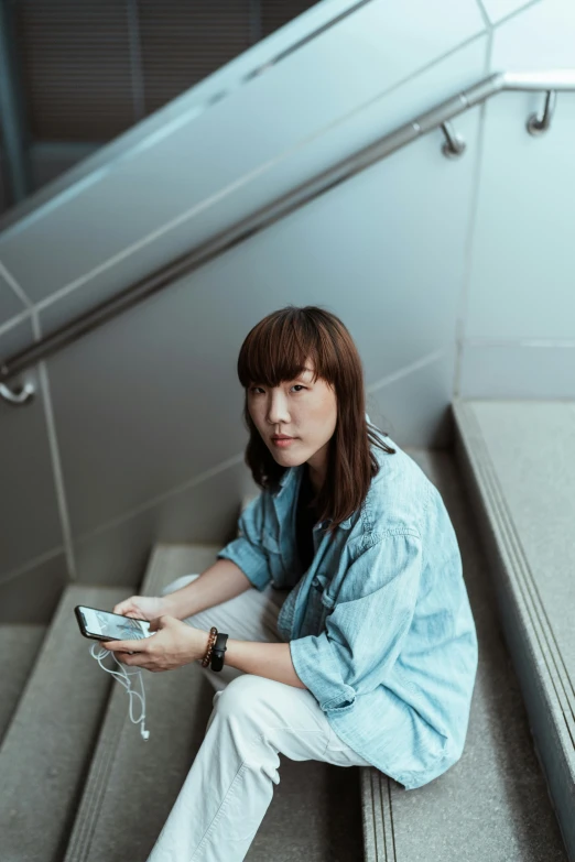 a woman sitting on a set of stairs holding a cell phone, inspired by Fei Danxu, trending on pexels, hyperrealism, wearing a light blue shirt, wearing headphones, asian human, with bangs