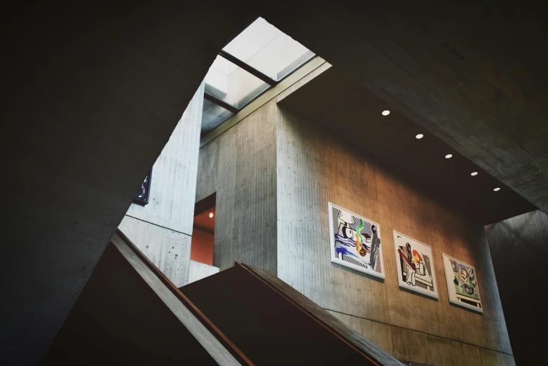 a staircase in a building with pictures on the wall, inspired by Tadao Ando, unsplash, visual art, concrete, concert, charles sheeler, inside a library