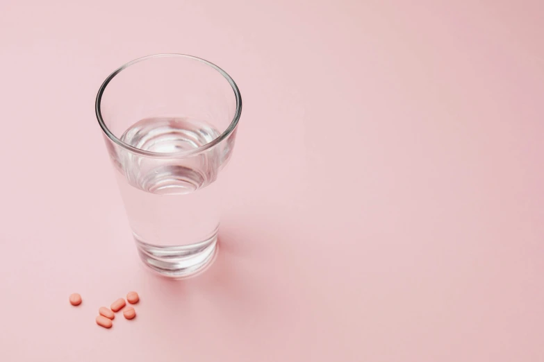 a glass of water and pills on a pink background, by Emma Andijewska, pexels, on a white table, 1/30, fan favorite, malnourished