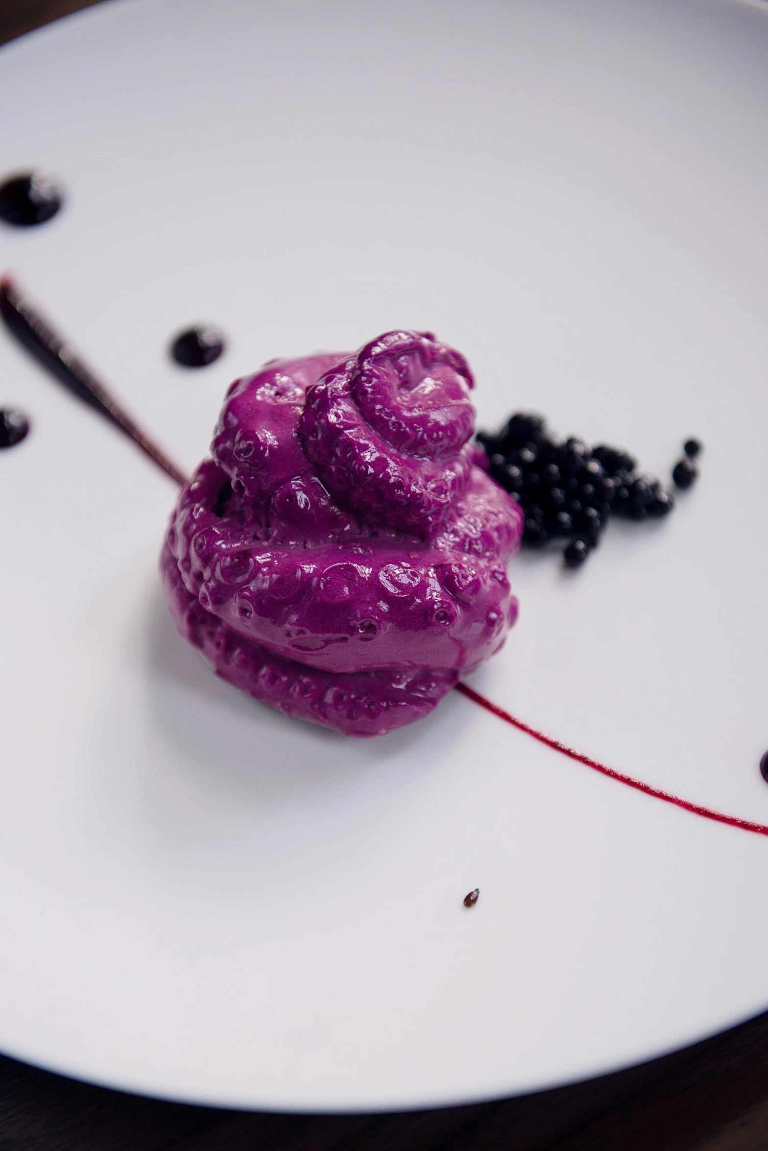 a purple dessert sitting on top of a white plate, a portrait, inspired by Anish Kapoor, unsplash, black slime, raspberry, ignant, carved from sapphire stone