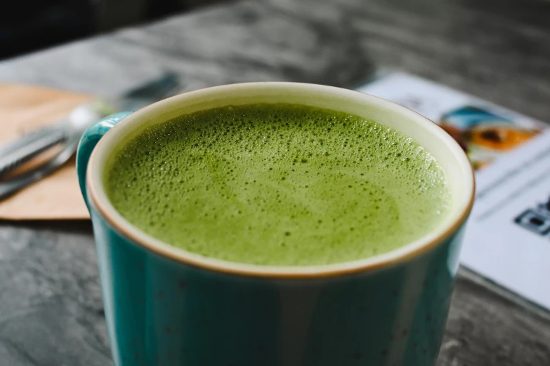 a cup of matcha sitting on top of a wooden table, detailed product image, zoomed in shots, full of colour, gooey skin