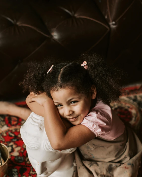 a little girl sitting on top of a bed, hugging each other, portrait featured on unsplash, brown skinned, sitting on couch