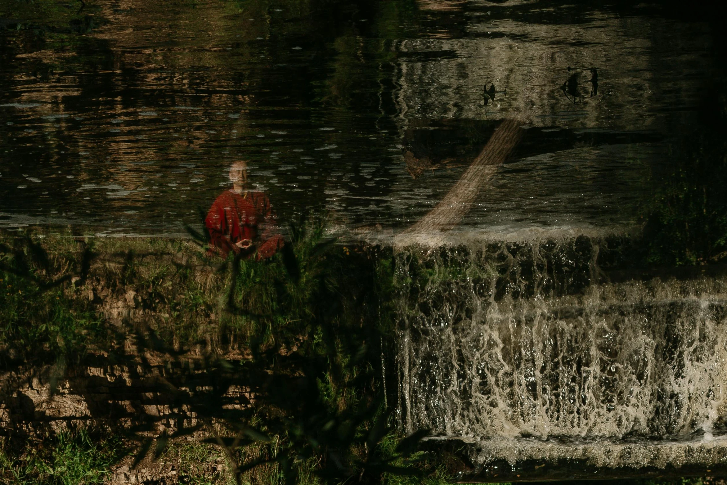 a man sitting on the edge of a waterfall, inspired by Anna Füssli, red reflections, zoomed out to show entire image, standing in a pond, photograph taken in 2 0 2 0