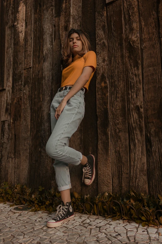 a woman leaning against a wooden wall, inspired by Elsa Bleda, trending on pexels, wearing pants and a t-shirt, full body cgsociety, ocher, teenage