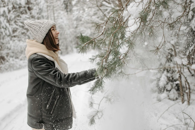 a woman standing next to a tree in the snow, pexels contest winner, dusting of snow, profile image, leather clothing, thumbnail