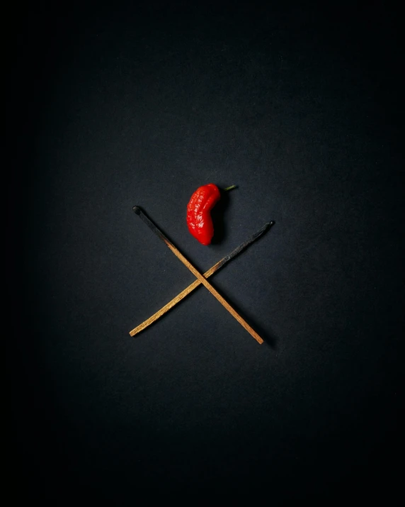 two matches and a red pepper on a black background, an album cover, by Adam Marczyński, pexels contest winner, x logo, crossed eyes, tiny sticks, cupid