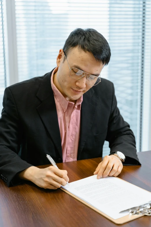 a man sitting at a table writing on a piece of paper, asian male, wearing a suit and glasses, professional image, panels