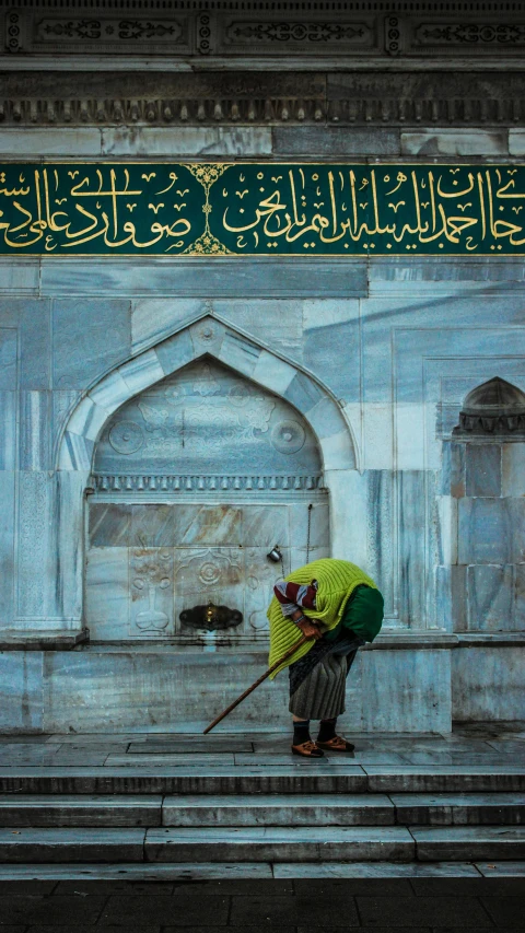 a man with a cane standing in front of a building, an album cover, inspired by Osman Hamdi Bey, unsplash contest winner, hurufiyya, featuring marble fountains, islamic calligraphy, wearing elaborate green and gold, getty images