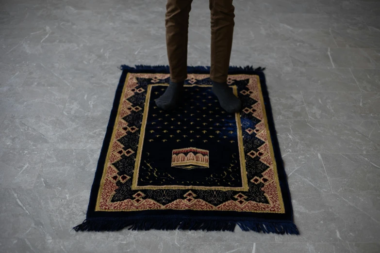 a person standing on a rug on the floor, hurufiyya, regal dark blue clothes, vintage - w 1 0 2 4, hyper realistic, praying