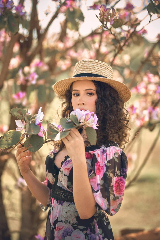 a woman holding a flower in front of a tree, curly haired, with hat, 2019 trending photo, brunette