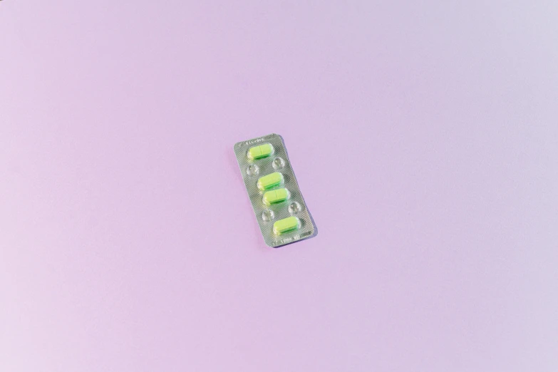 a pill pack sitting on top of a pink surface, by Amelia Peláez, pexels, synchromism, pale green backlit glow, green bioluminescent chrometype, pigtail, small eyes