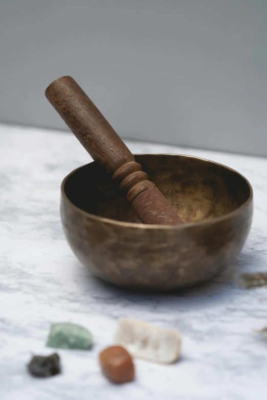 a close up of a bowl with a wooden stick in it, by Caroline Lucy Scott, trending on pexels, meditating pose, brass copper, official product photo, bells