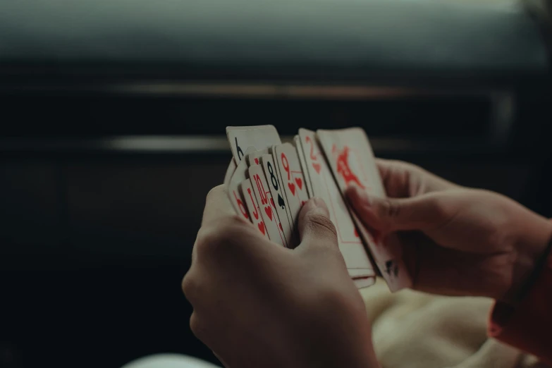 a person holding playing cards in their hands, by Emma Andijewska, pexels contest winner, piled around, driving, thumbnail, low quality photo